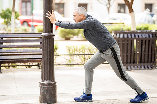 Phoenix Man Who Had Shoulder Pain Treatment in Tolleson AZ Stretching Against a Pole Before Jogging